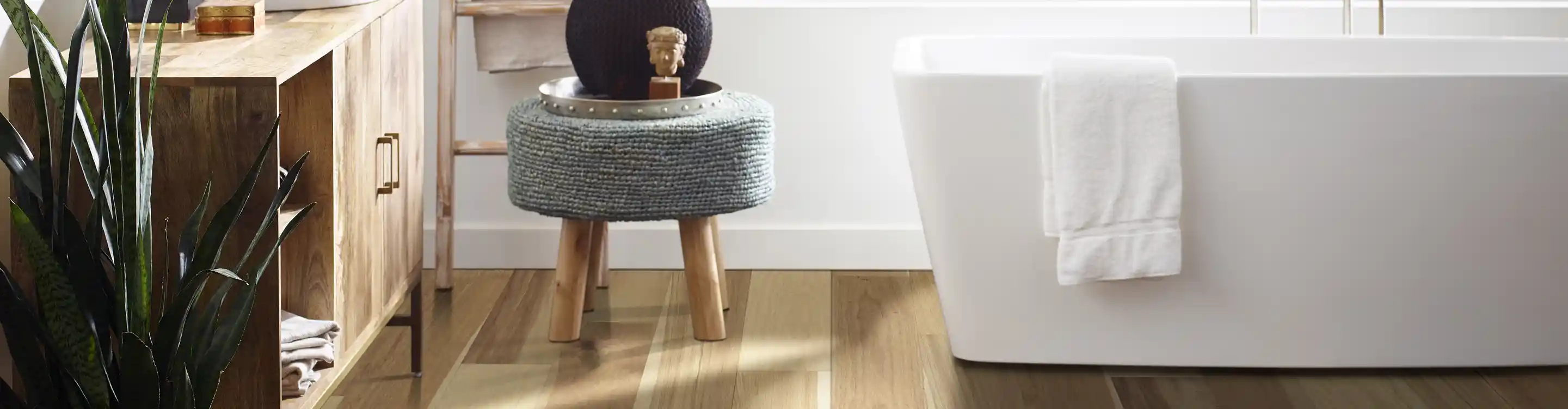 light wood look flooring in bathroom with white soaker tub and brown vanity